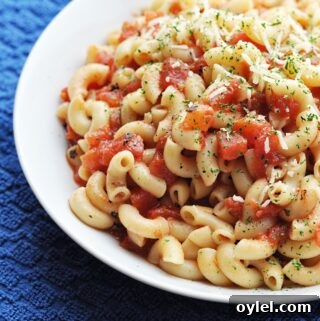 Cooked macaroni with diced tomatoes in white bowl ready to eat.