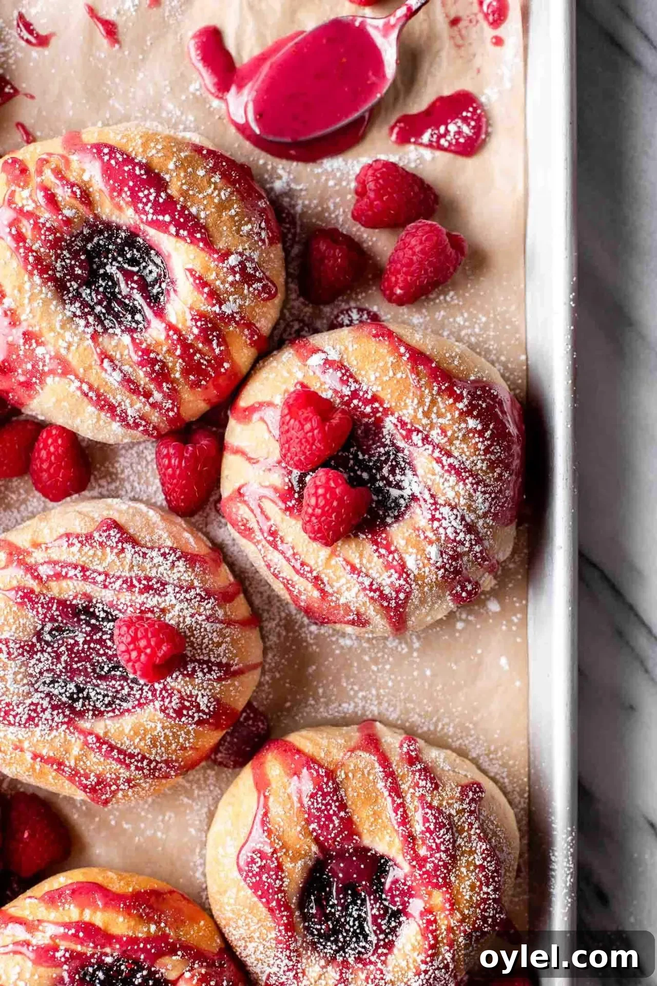 Fluffy Raspberry Buns Recipe 2 baked raspberry donuts on parchment lined baking sheet topped with icing and a light dusting of powdered sugar