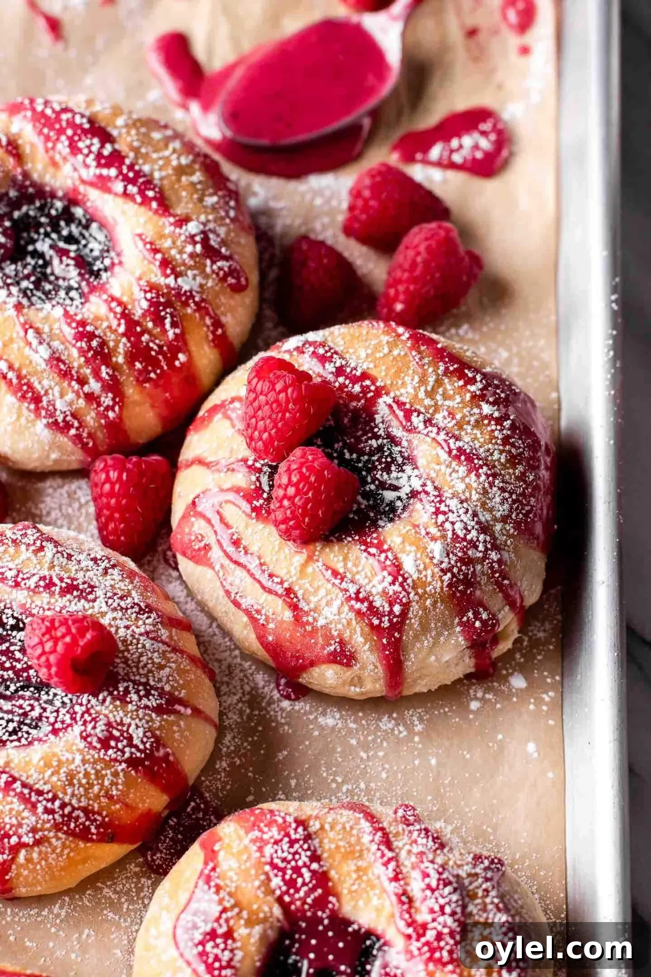 Fluffy Raspberry Buns Recipe 3 baked raspberry donuts on parchment lined baking sheet topped with icing and a light dusting of powdered sugar