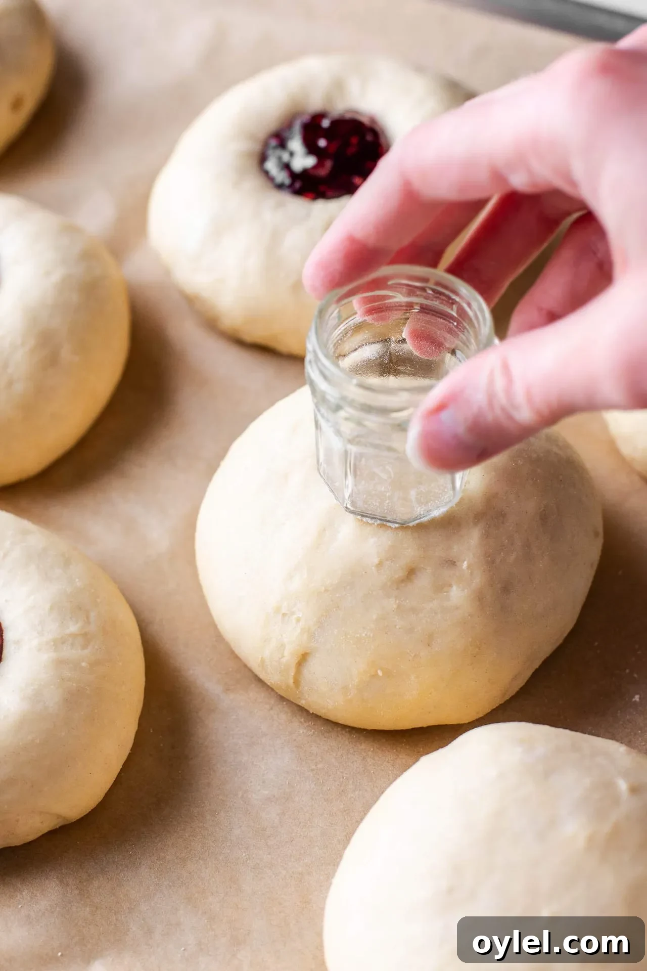 Fluffy Raspberry Buns Recipe 5 baked raspberry donuts dough balls on parchment lined baking sheet with jar pushing center indent in buns