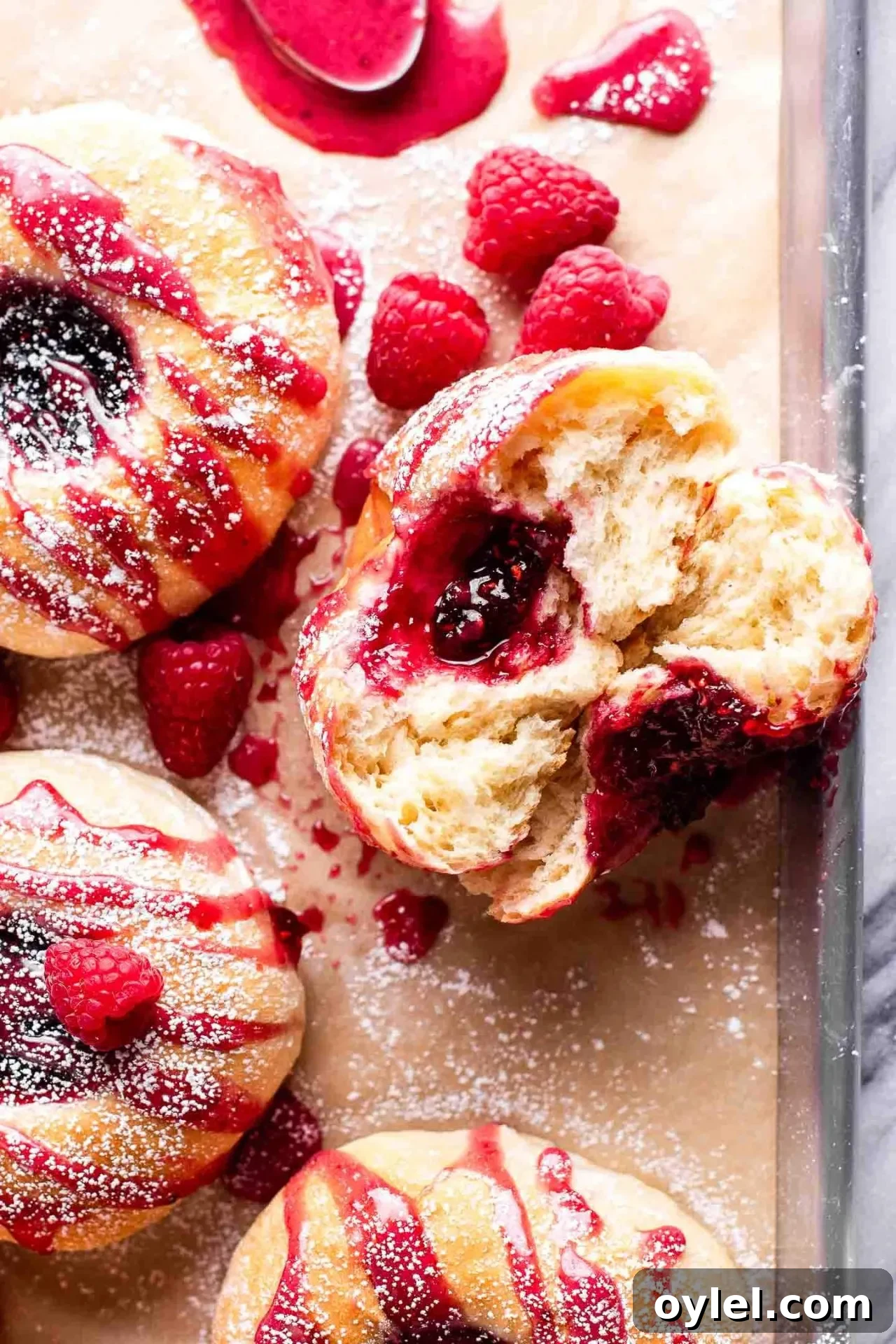 Fluffy Raspberry Buns Recipe 6 baked raspberry donuts on parchment lined baking sheet topped with icing and a light dusting of powdered sugar