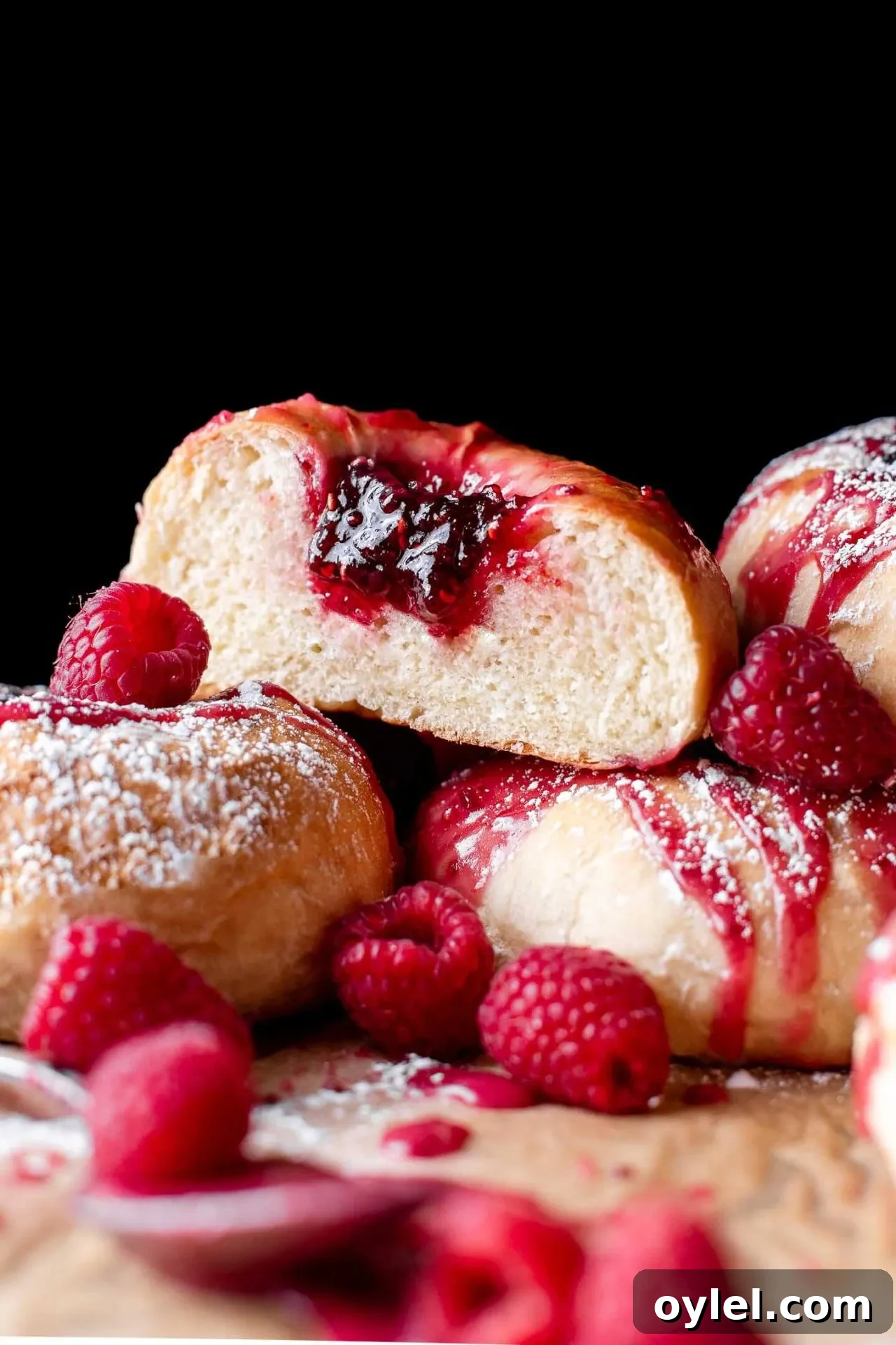 Fluffy Raspberry Buns Recipe 7 baked raspberry donuts on parchment lined baking sheet topped with icing and a light dusting of powdered sugar