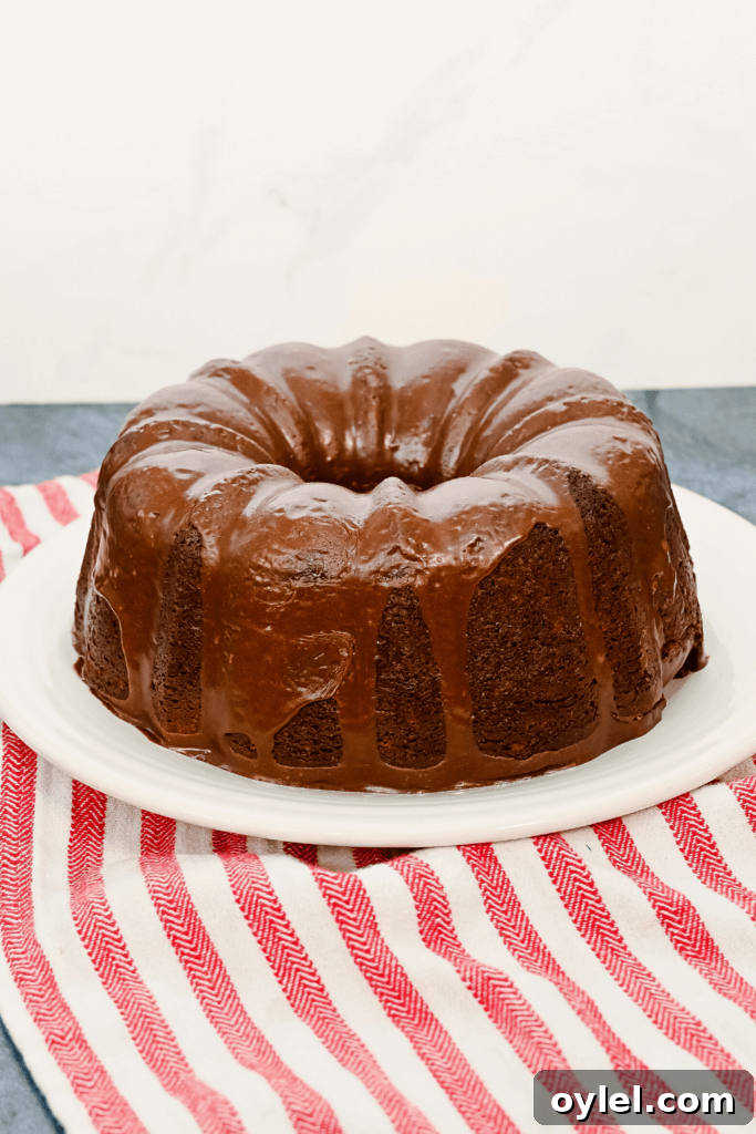 Hershey Bar Chocolate Cake on a white plate, drizzled in melted chocolate frosting, on a red striped towel.