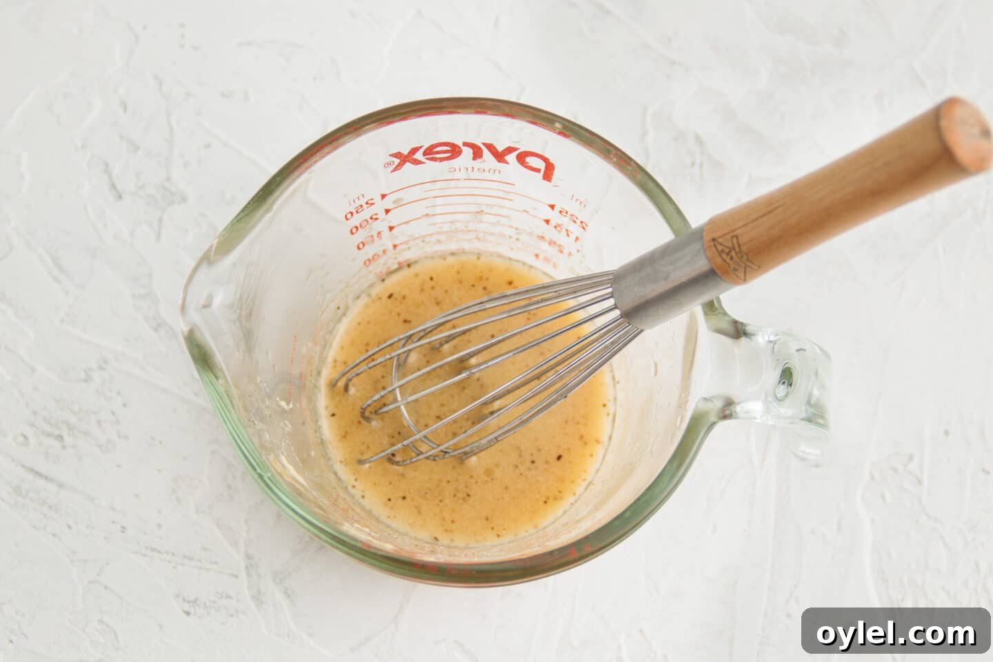 Picture of measuring cup with vinaigrette and whisk.