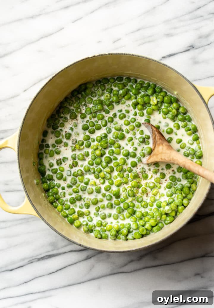 easy creamed peas in a yellow pot with a wooden spoon
