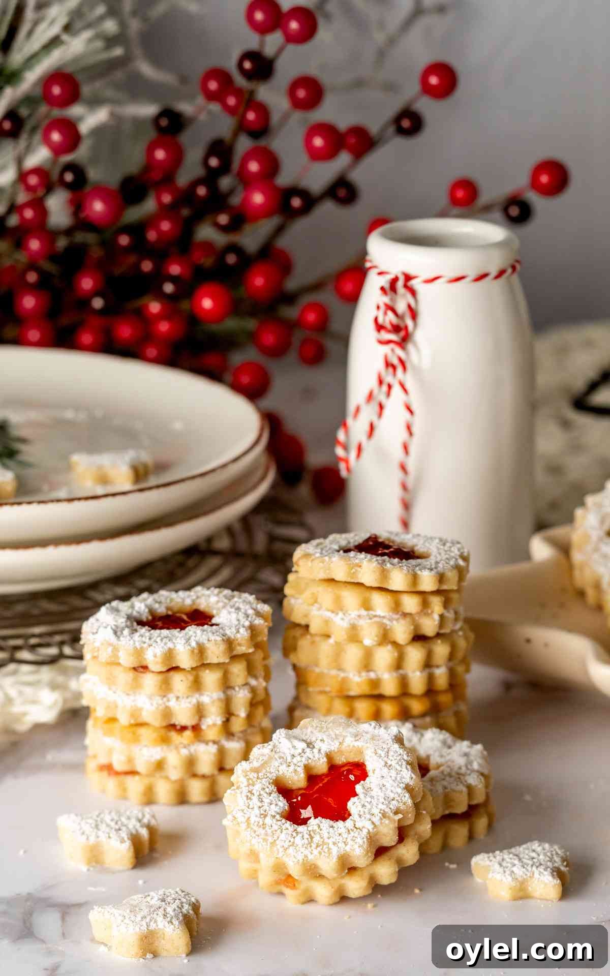 Stacked Raspberry Linzer Tarts in front of a plate and milk.