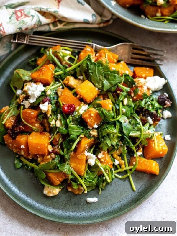 Green plate with salad and roasted butternut squash on it. Silver fork on the side.