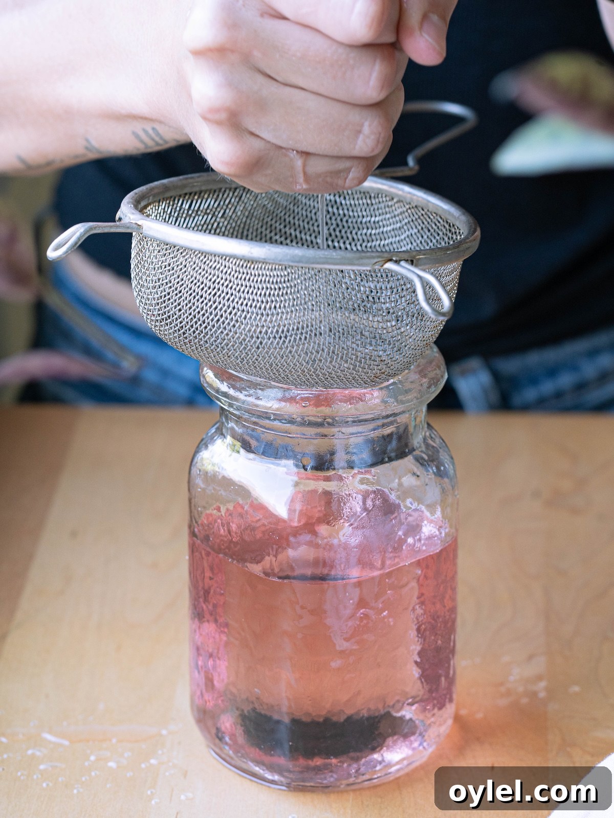 How to Make Rose Simple Syrup for Cocktails and Desserts 7 Squeezing simple syrup out of cheesecloth over a strainer