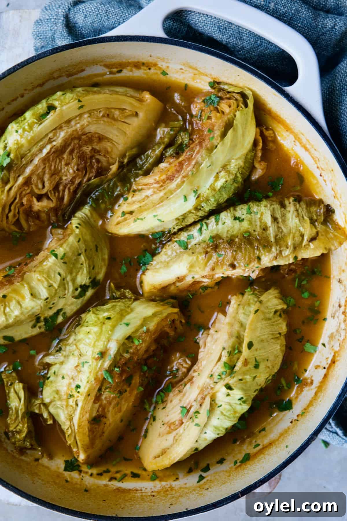 Cider Vinegar Braised Cabbage Wedges in white enamel cast iron skillet garnished with fresh parsley.