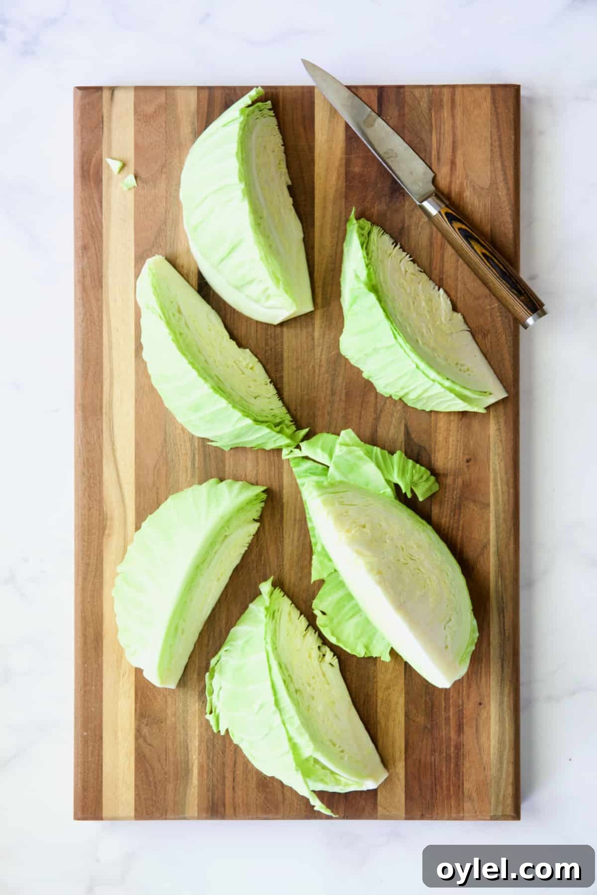 Six cabbage wedges on wood cutting board with knife.