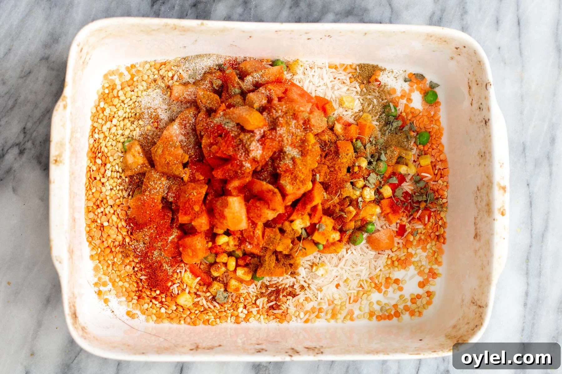 spices being added to rice and lentils in a casserole dish to make kitchari casserole