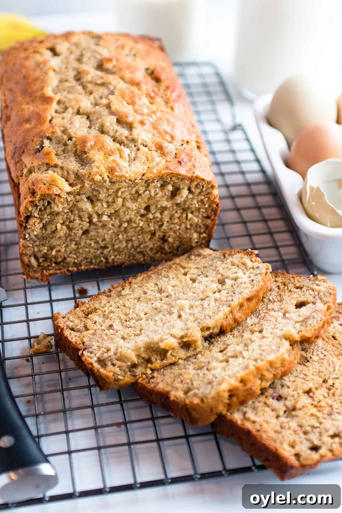 Moist Sourdough Discard Banana Bread Recipe 2 Cooling rack with a loaf of sourdough banana bread, eggs, bananas and a glass of milk.
