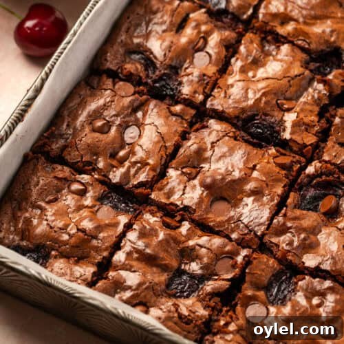 A pan of cherry chocolate brownies sitting on a table next to a bowl of cherries.