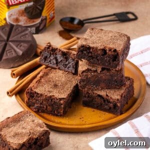 Delicious homemade chocolate brownies stacked on a plate with cinnamon sticks.
