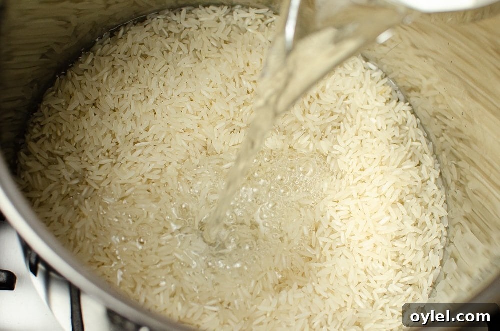 Authentic Jasmine Sticky Rice Recipe from Thailand 10 Water being poured on top of the rice in a silver cooking pot