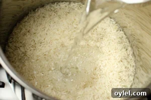Authentic Jasmine Sticky Rice Recipe from Thailand 5 Water being poured on top of the rice in a silver cooking pot