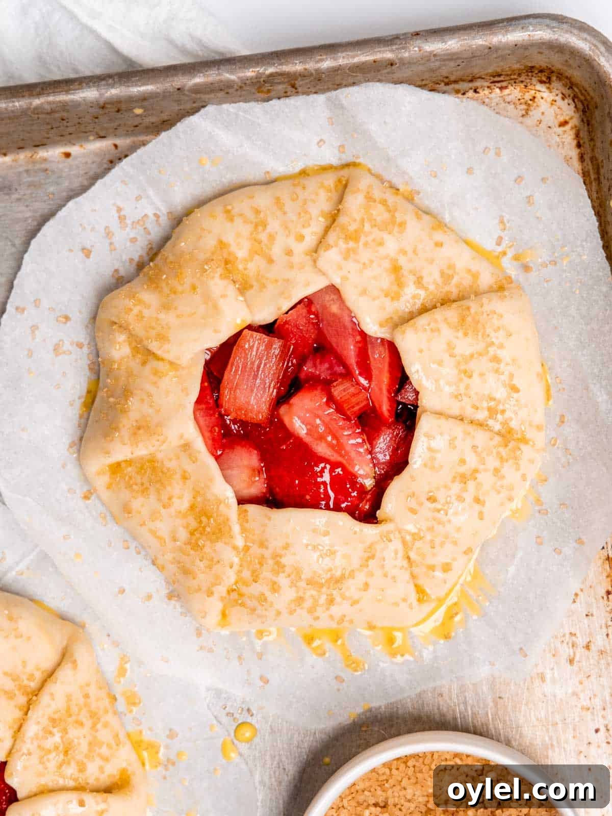 An unbaked strawberry rhubarb galette on a baking sheet with parchment paper.