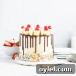 frosted banana split cake in front of a stack of plates and a bowl of strawberries
