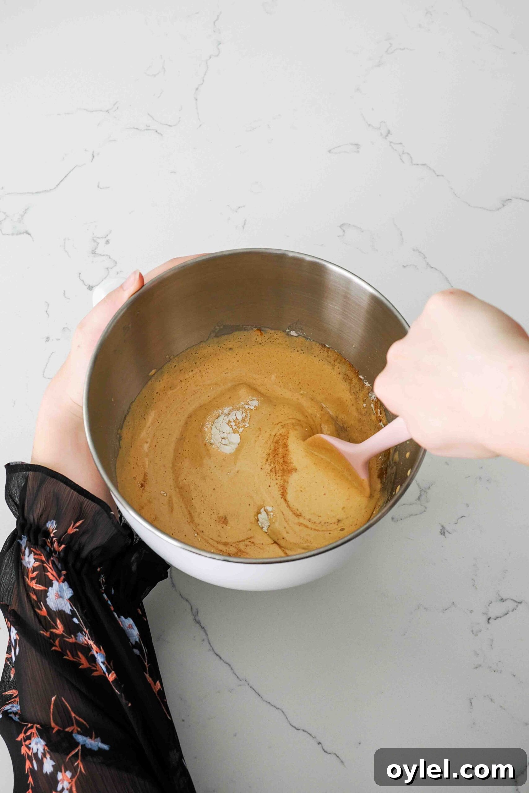A spatula folds dry ingredients into madeleine batter.