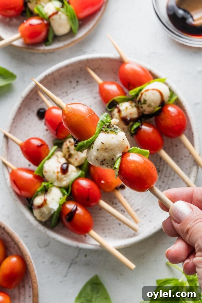 Caprese Skewers with Balsamic Glaze 5 Close up of a hand lifting a Caprese skewer from a small appetizer plate.
