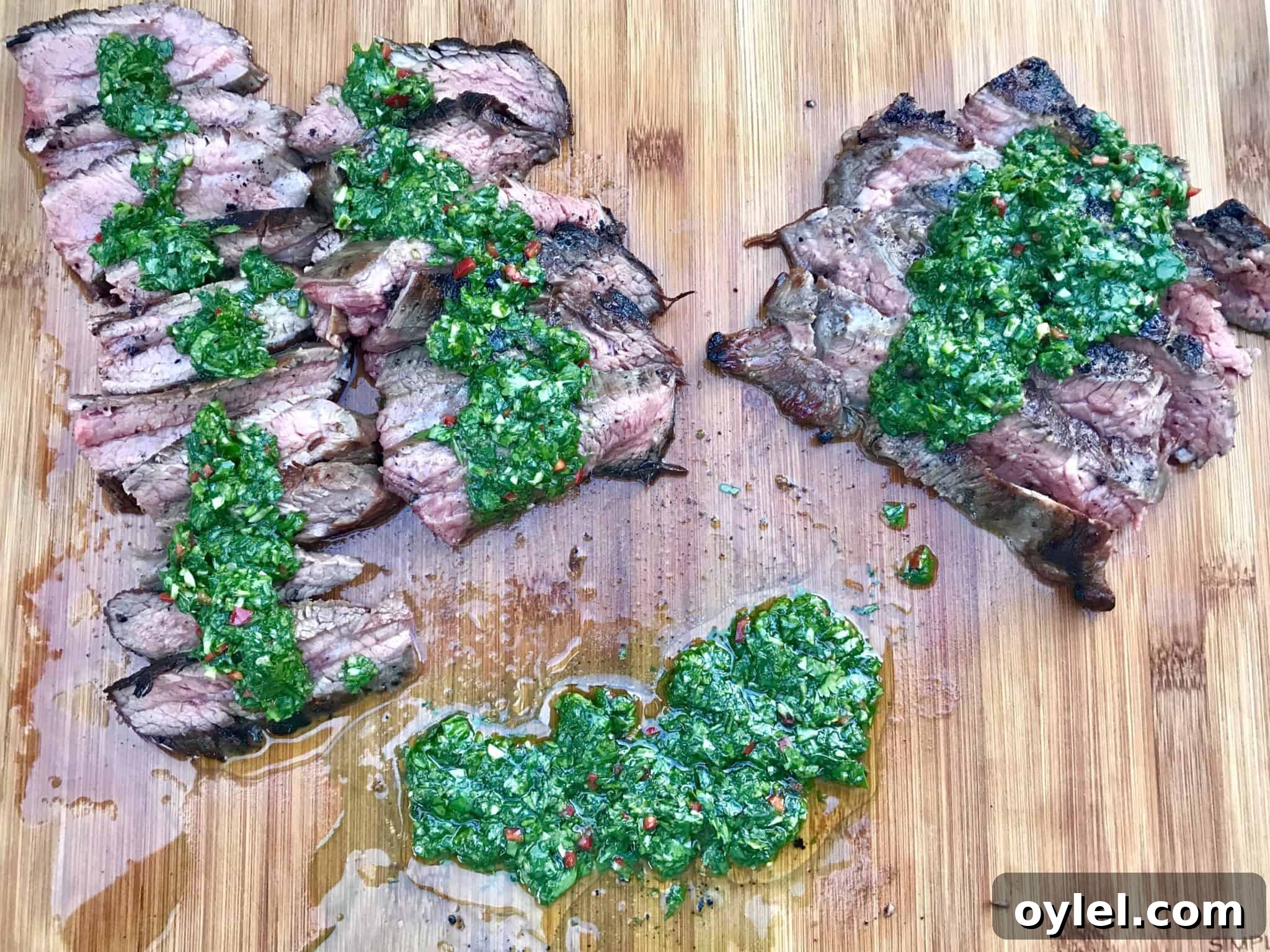 Chimichurri Sauce on top of multiple slices of steak on wooden cutting board overhead shot