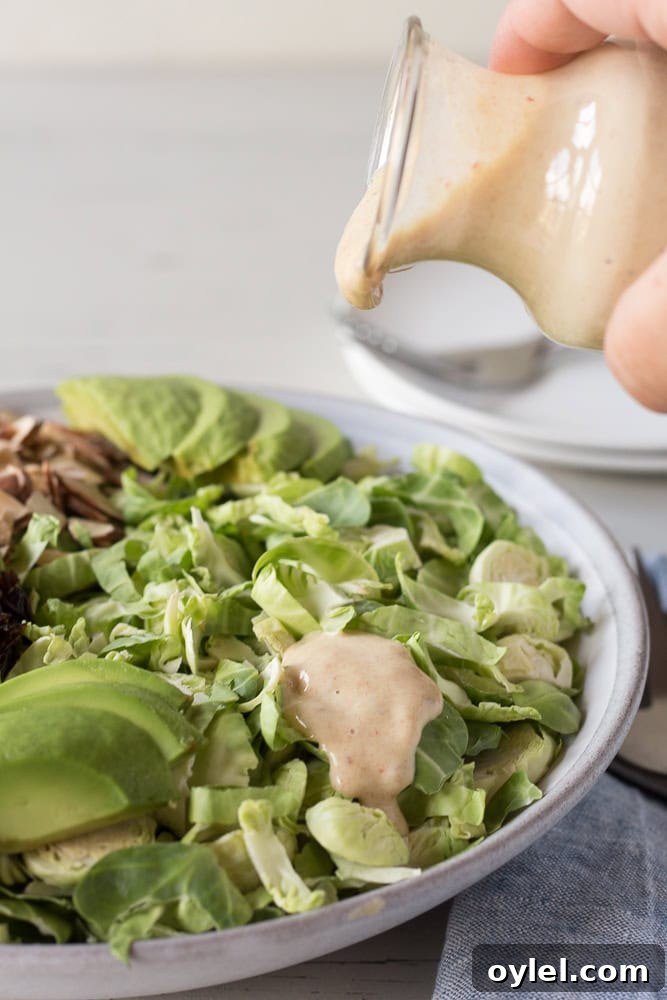 a hand pouring date dijon dressing over a salad