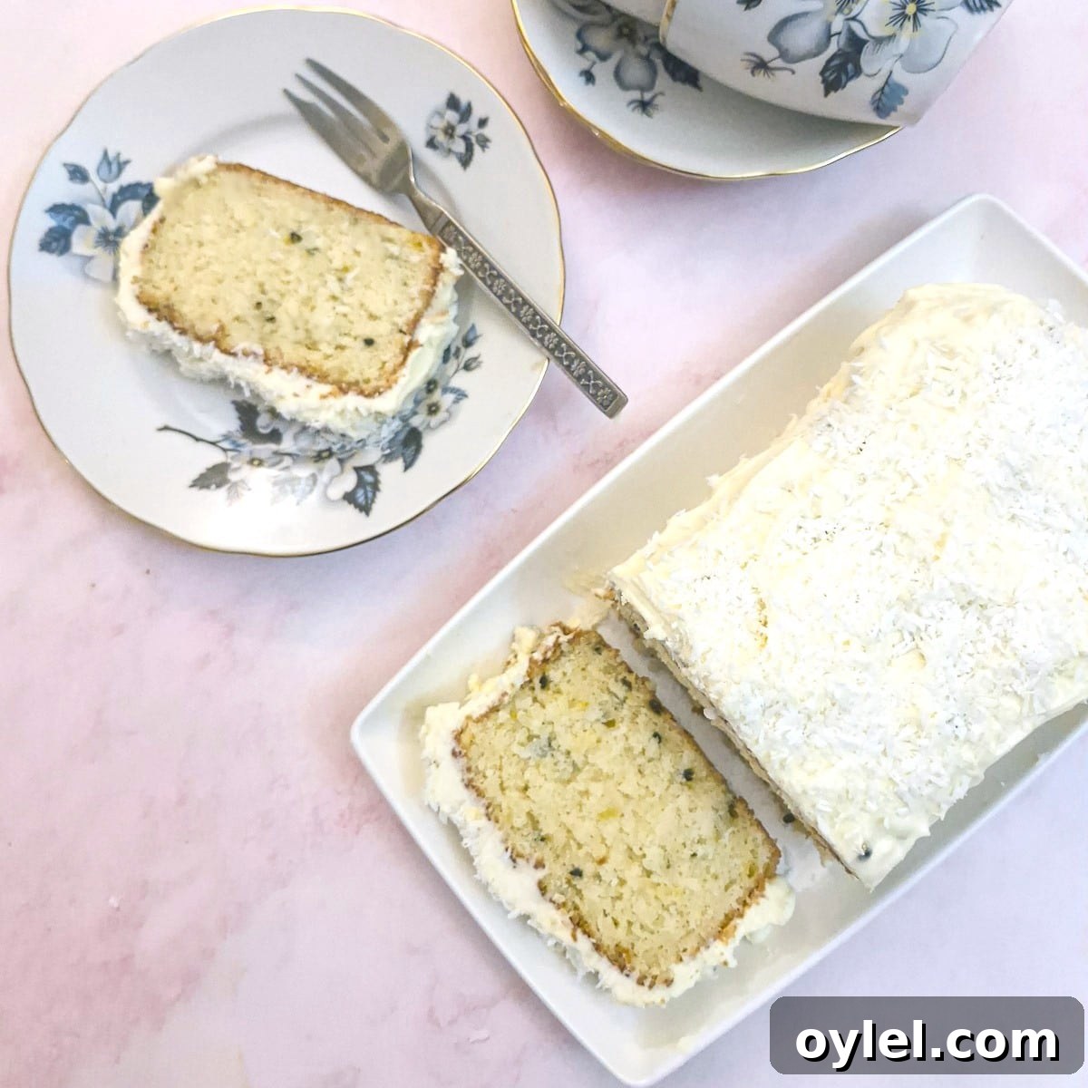 Overhead shot of a slice of coconut loaf cake on a small plate with the remaining whole cake on a serving plate.