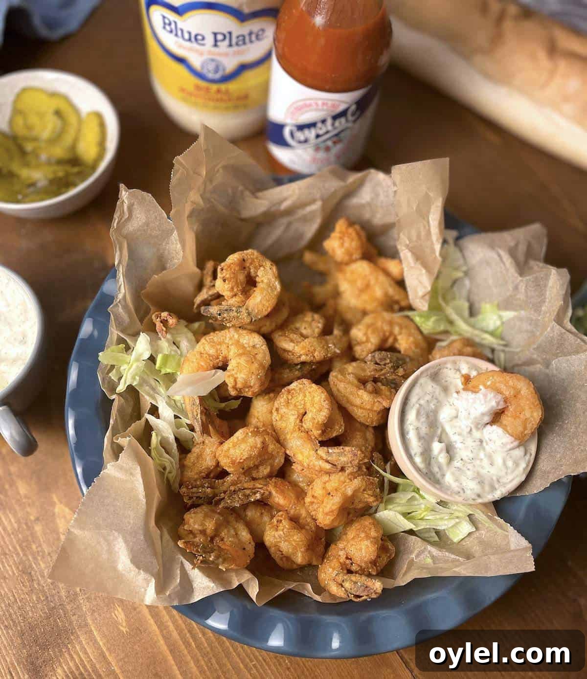 A small bowl of crispy fried shrimp with shredded lettuce, tartar sauce, and crystal hot sauce.