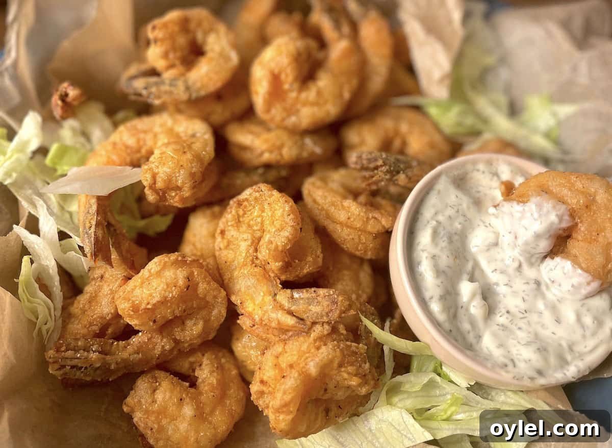 An up close image of crispy fried shrimp with the tails on and a small bowl of tartar sauce.