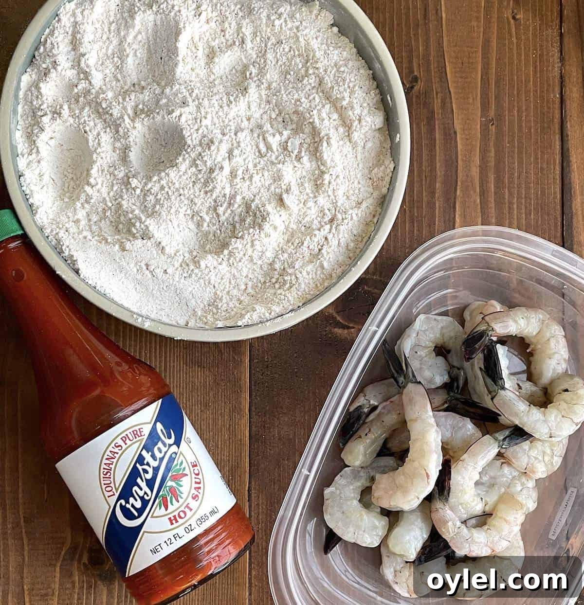 A bowl of crystal hot sauce, a bowl of raw shrimp, and a bowl of shrimp breading.
