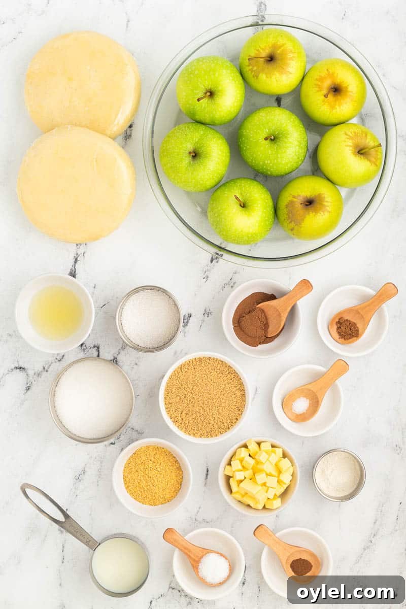Ingredients for a baking recipe arranged on a marble surface, including green apples, dough, sugar, spices, flour, butter, lemon juice, and other measured ingredients in bowls and measuring cups.