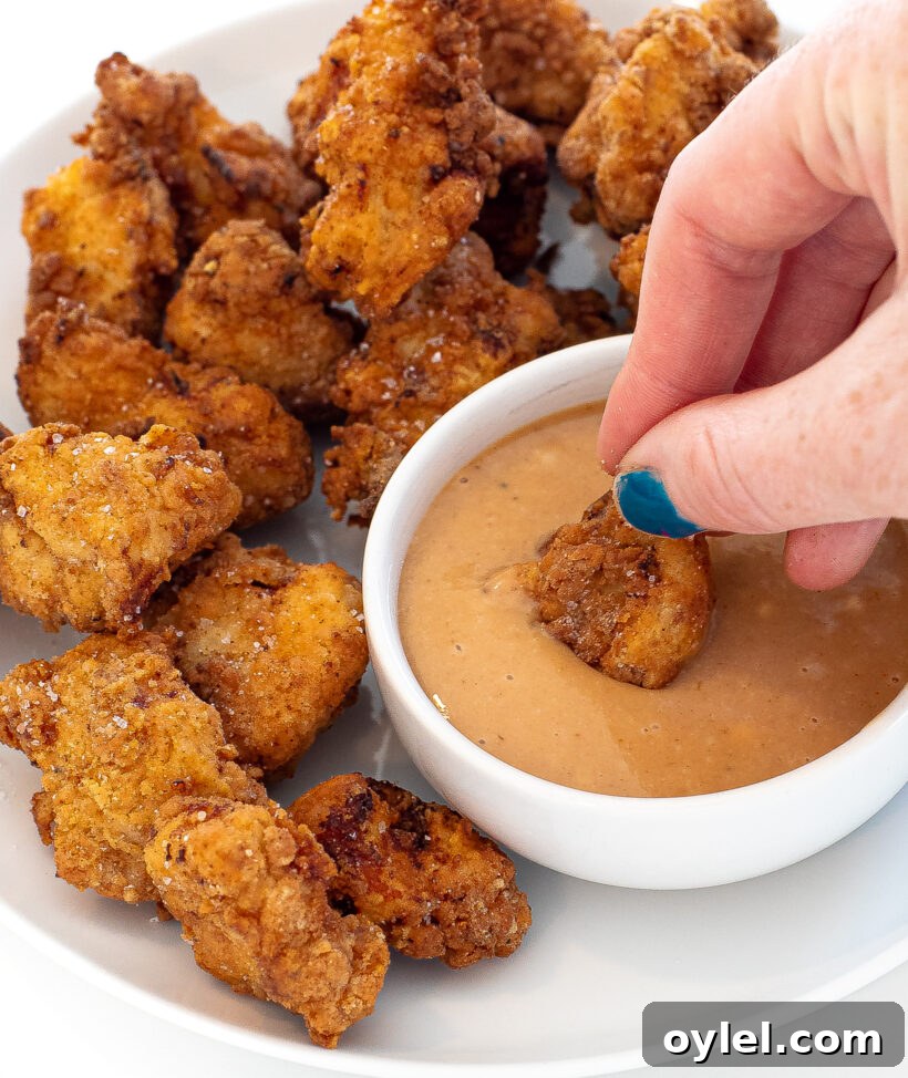 Hand dipping a chicken nugget in a small bowl of sauce with more nuggets next to it.