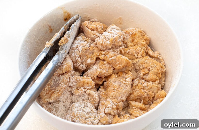 Raw chicken pieces being coated in flour and spices in a mixing bowl.