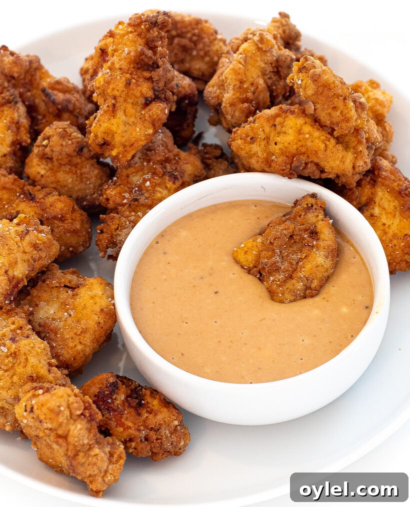 Chick fil a nuggets on a plate with one chicken nugget swimming in the sauce.