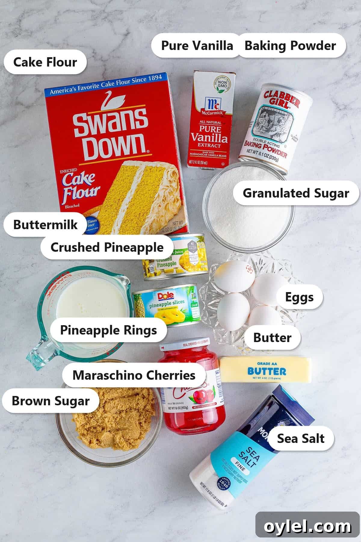 Pineapple Upside Down Cupcakes ingredients including cake flour, butter, sugar, eggs, buttermilk, pineapple, and cherries labeled on a counter.