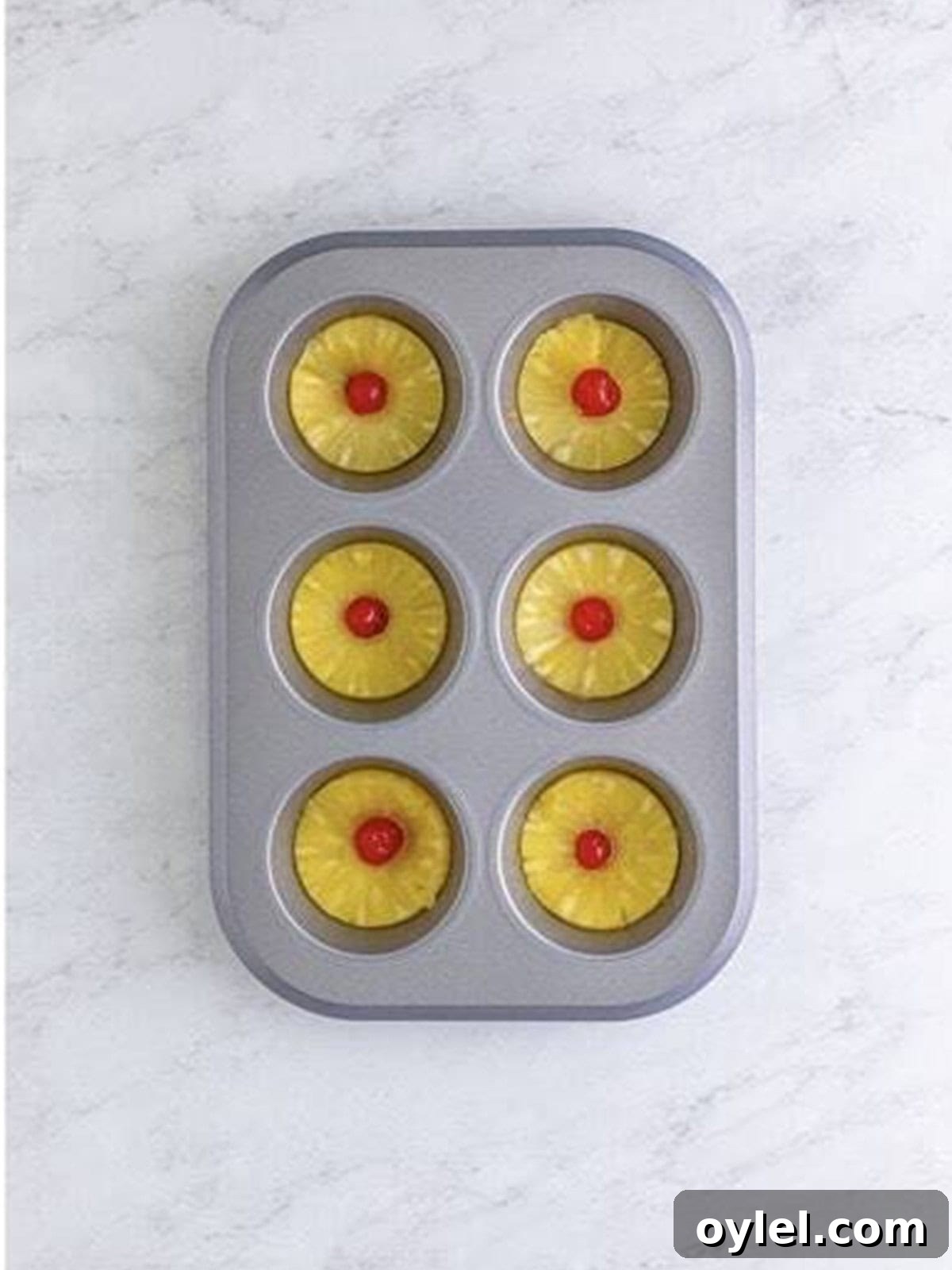 Pineapple rings and maraschino cherries placed over the sauce in a muffin tin.