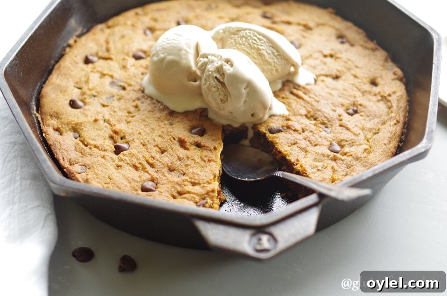 a side view of gluten free pumpkin chocolate chip skillet cookie in a cast iron skillet topped with three scoops of vanilla ice cream