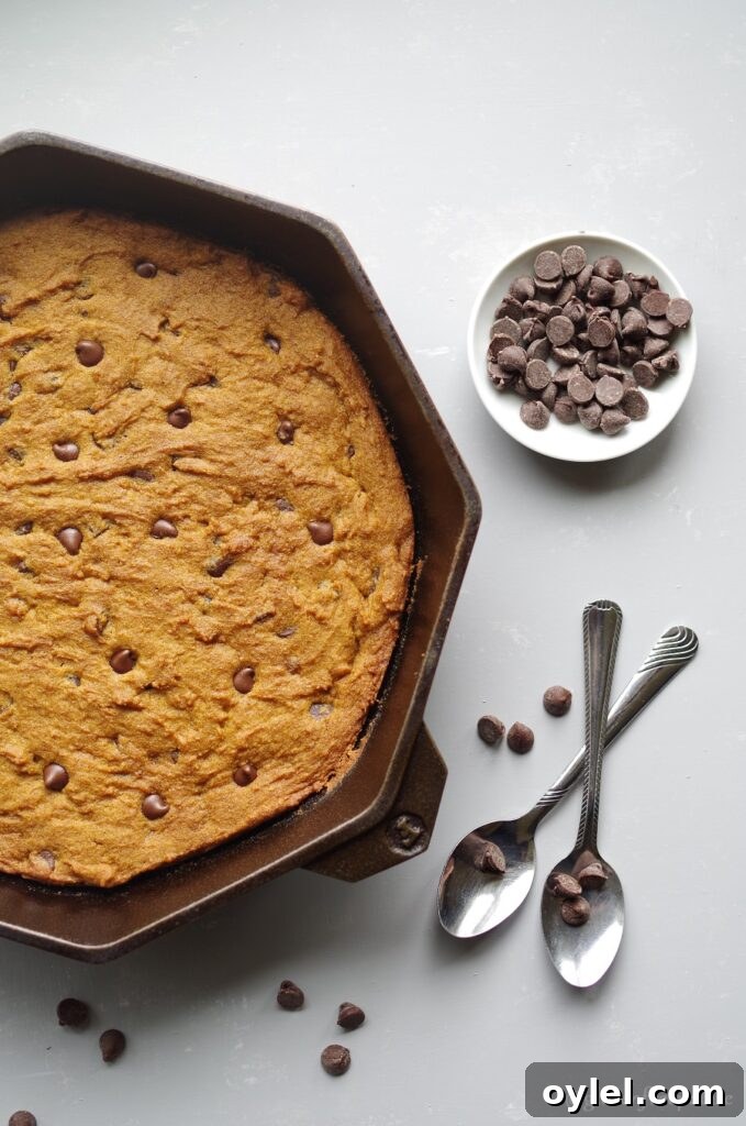 gluten free pumpkin chocolate chip skillet cookie in a cast iron skillet next to two spoons and a bowl of chocolate chips