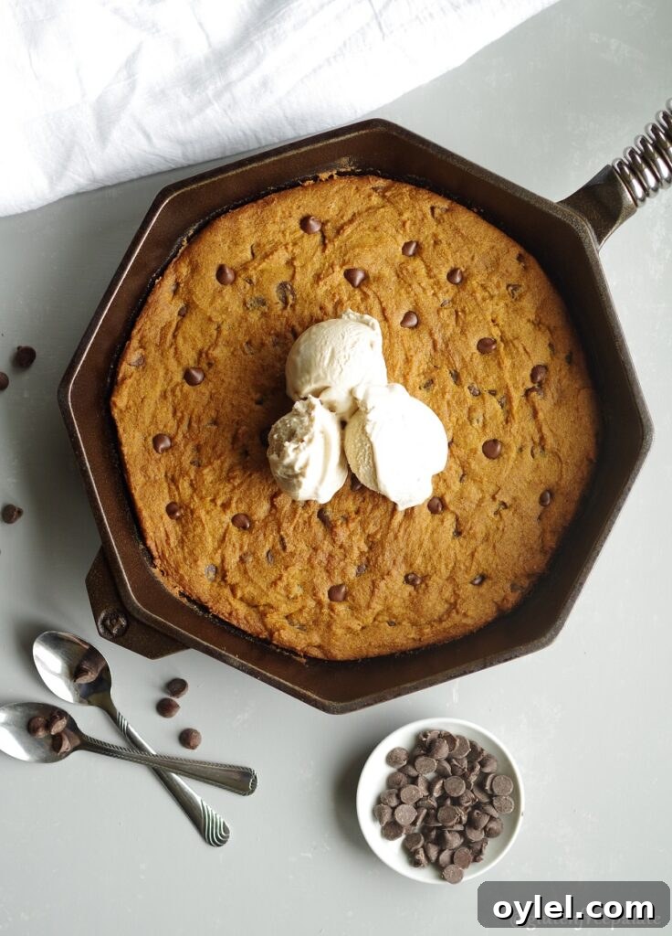 gluten free pumpkin chocolate chip skillet cookie in a cast iron skillet topped with three scoops of vanilla ice cream