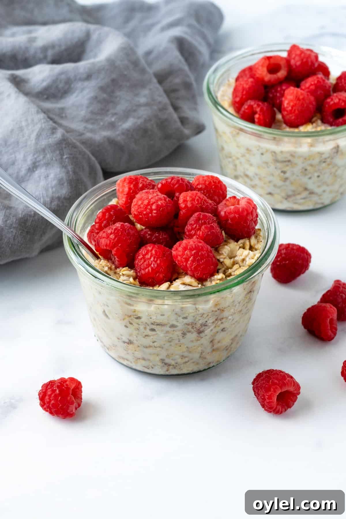 Creamy Raspberry Overnight Oats Recipe 2 Overnight Oats with Raspberries on a marble countertop with raspberries spread on the table.