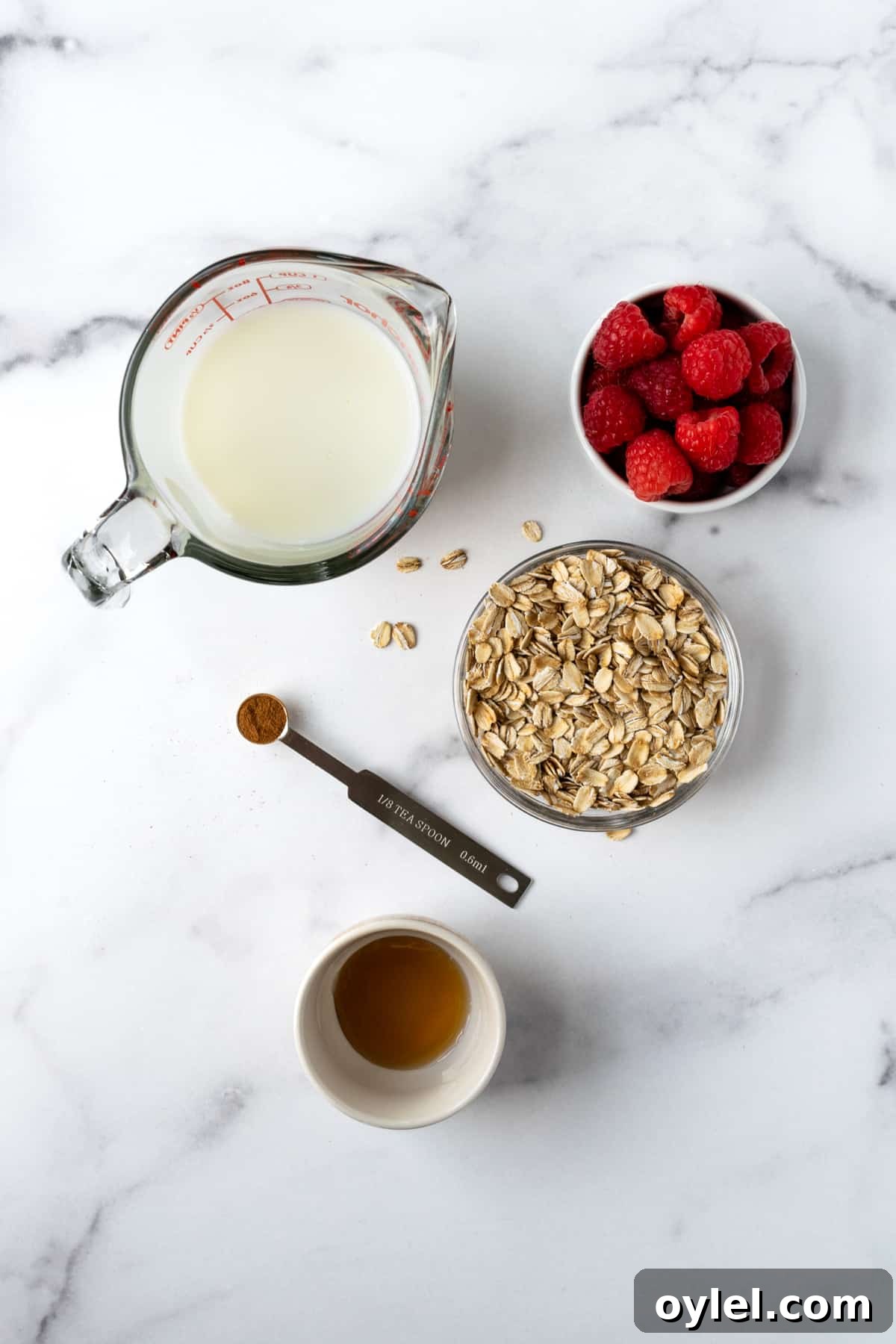Creamy Raspberry Overnight Oats Recipe 3 Milk, Oats, Raspberries, Cinnamon, and Maple Syrup in prep bowls on a marble countertop for overnight oats.