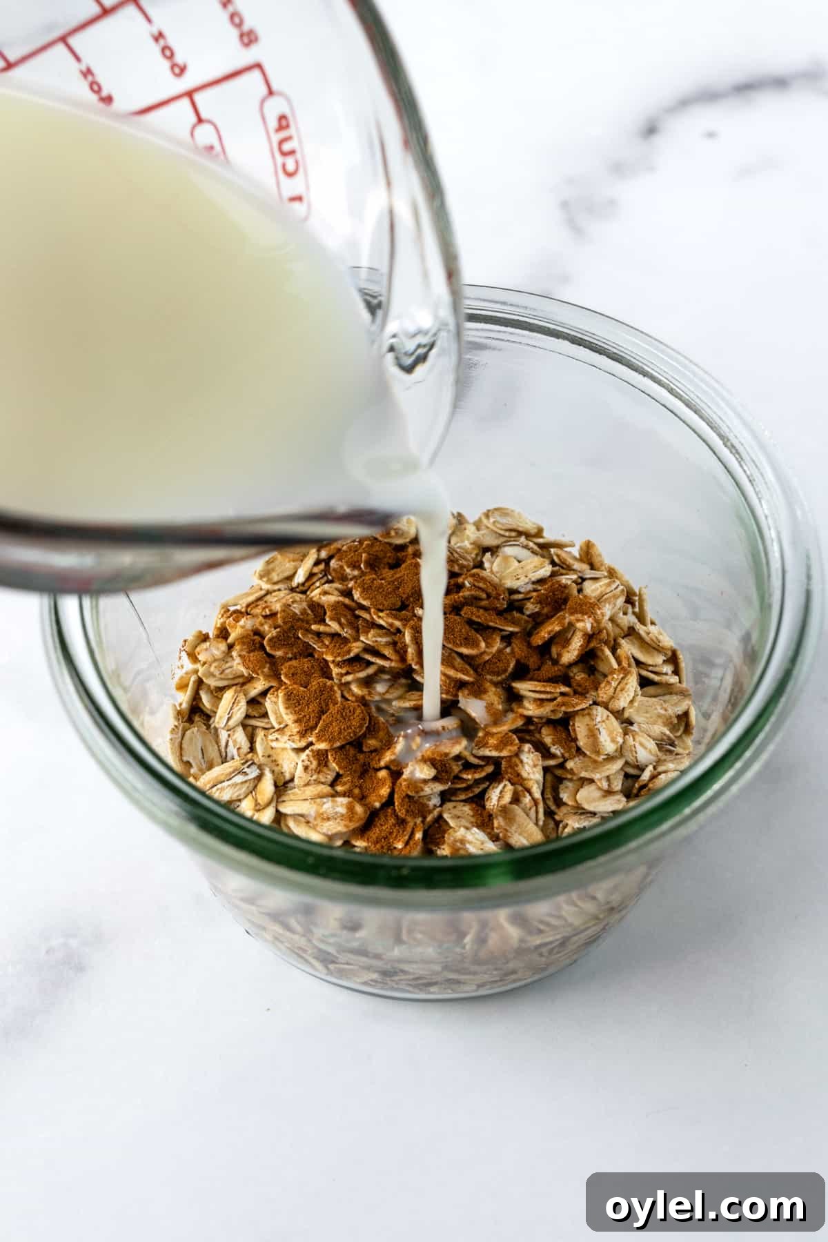Creamy Raspberry Overnight Oats Recipe 4 Pouring milk from a measuring cup into a jar full of overnight oats ingredients.