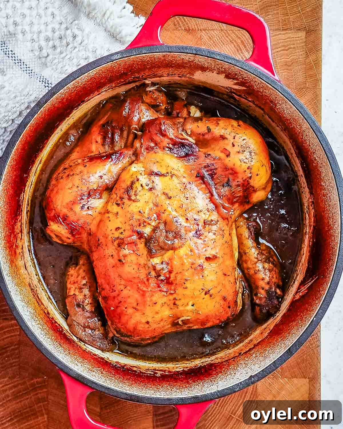 Balsamic Chicken with Caramelized Onions and Garlic 7 A large deep Dutch oven with red handles containing a whole baked chicken in a dark balsamic gravy.