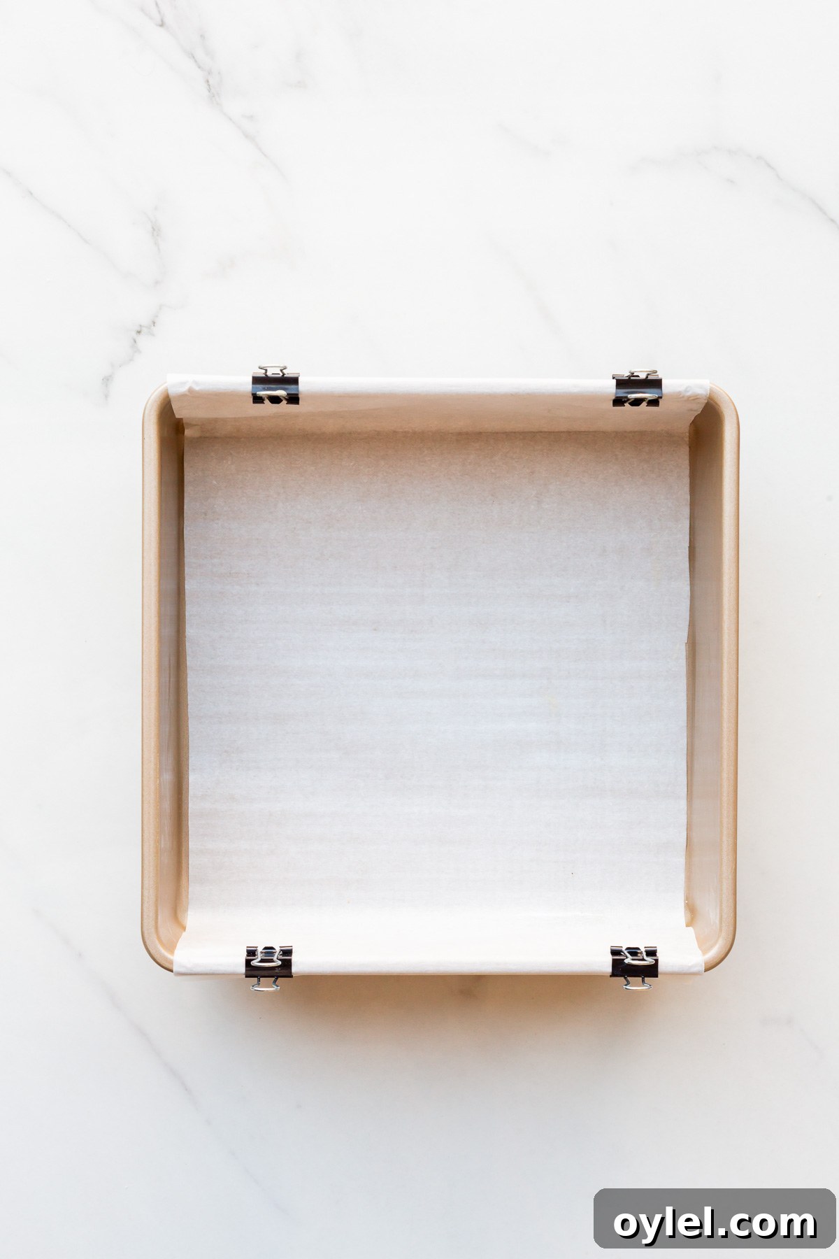 Apple Crisp Bars Recipe with Oat Streusel 7 A square metal baking pan lined with parchment paper with an overhang secured in place with binder clips.