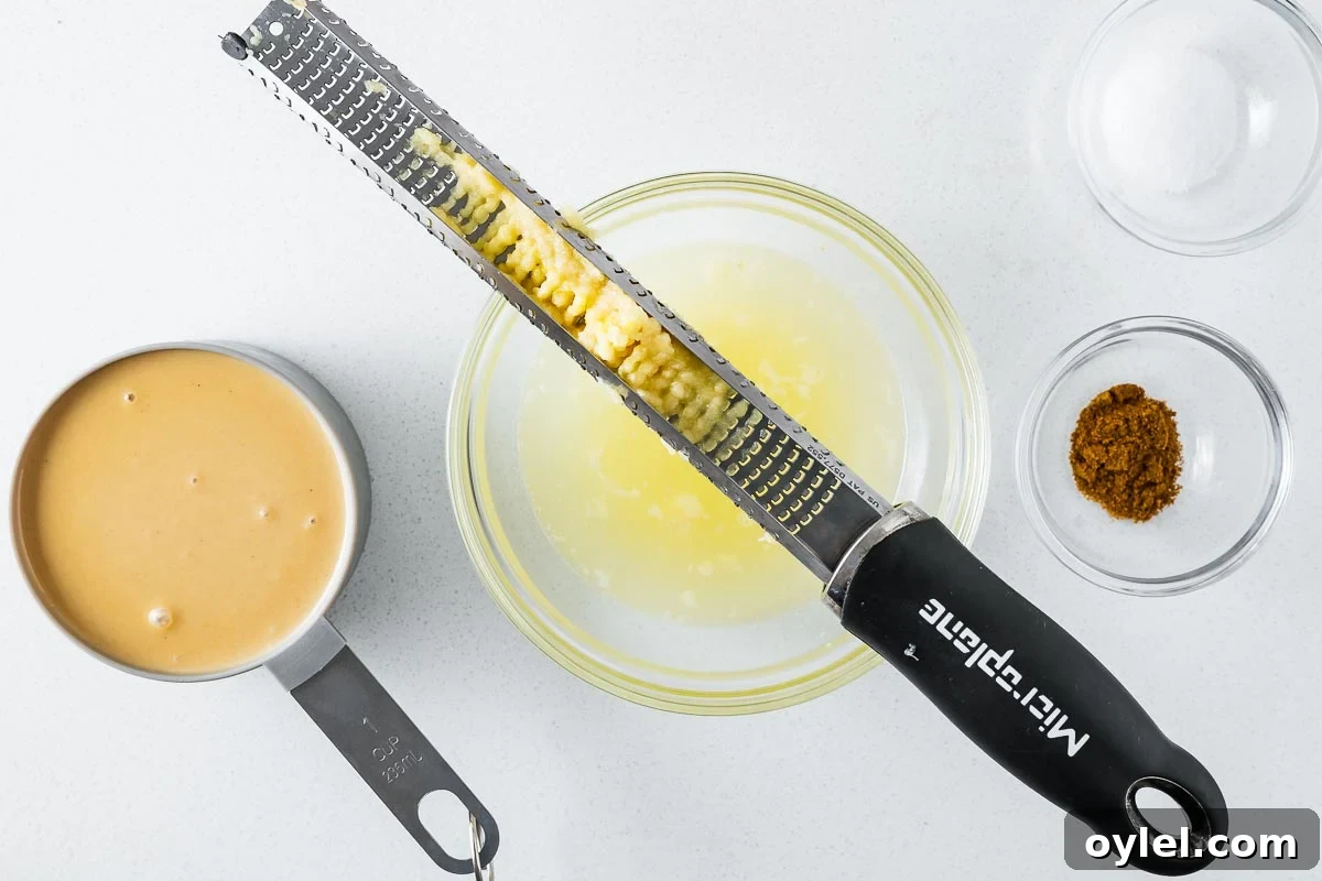 Lemon Tahini Sauce Recipe: 5 Flavor Variations 3 Garlic grated with a Microplane viewed from above with more tahini sauce ingredients.