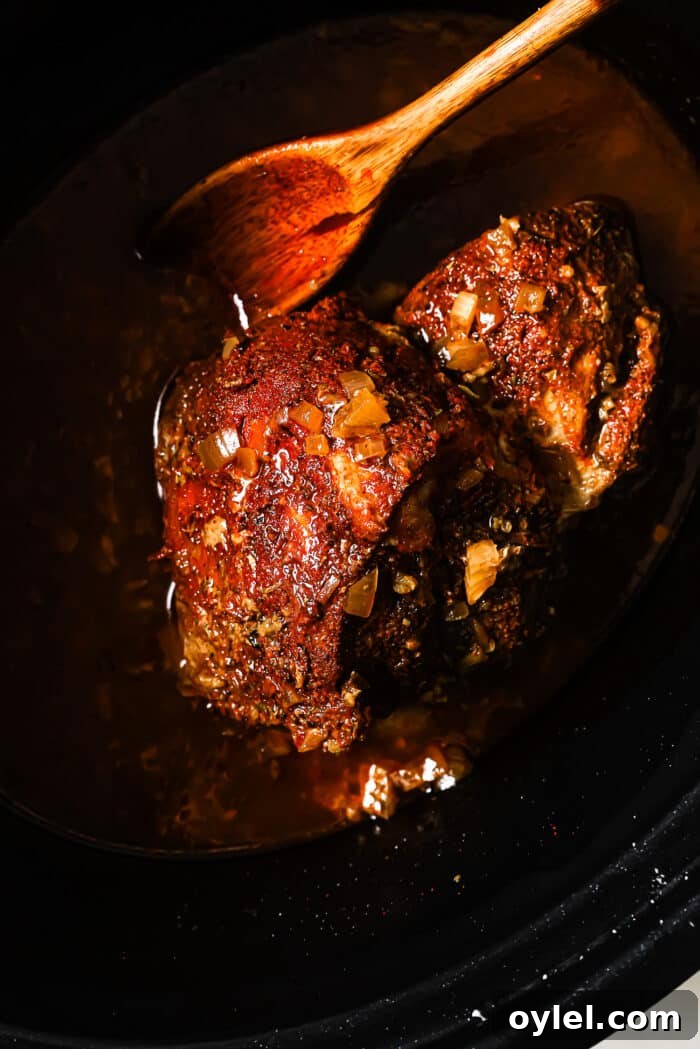 Cooked pork in a slow cooker with a wooden spoon in it. 
