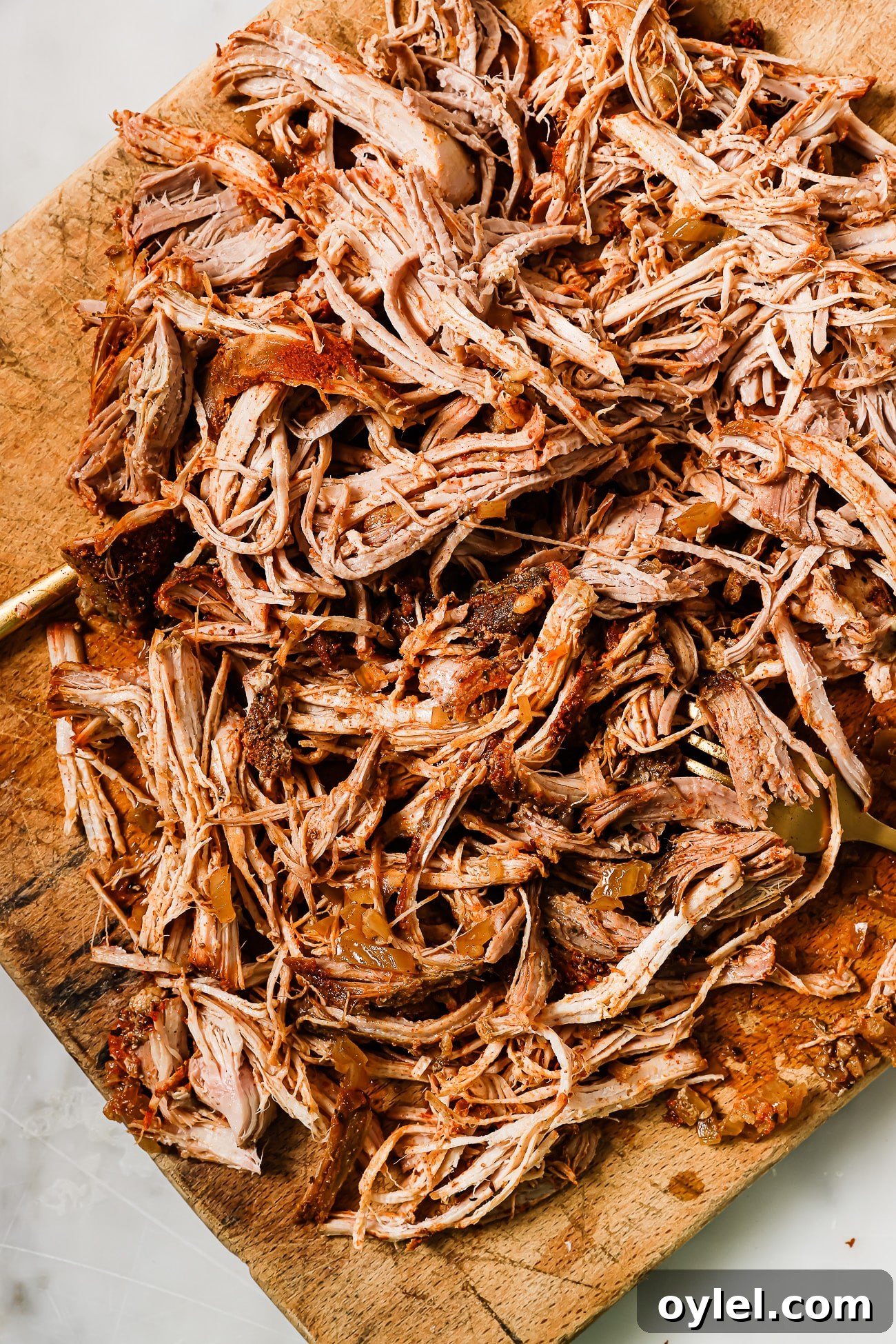 An overhead view of pulled pork on a wooden cutting board. 