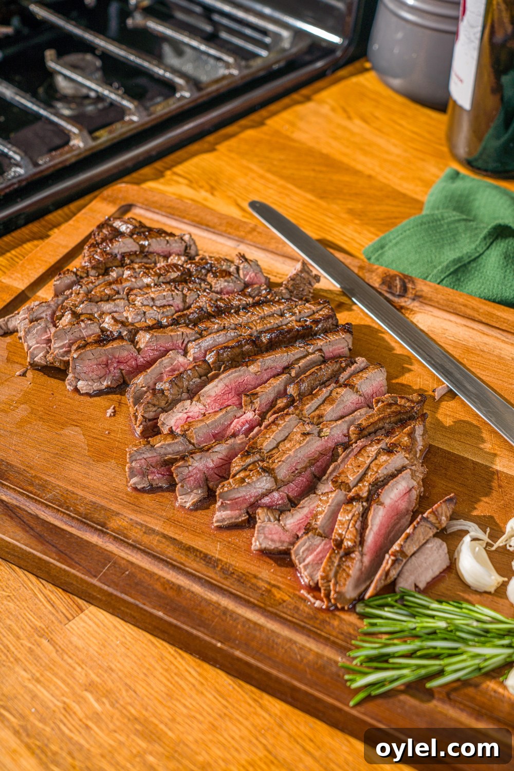 London Broil Marinade Recipe for Tender, Flavorful Steak 2 A wooden board with sliced London broil served with garlic and rosemary. There is a knife on the board.