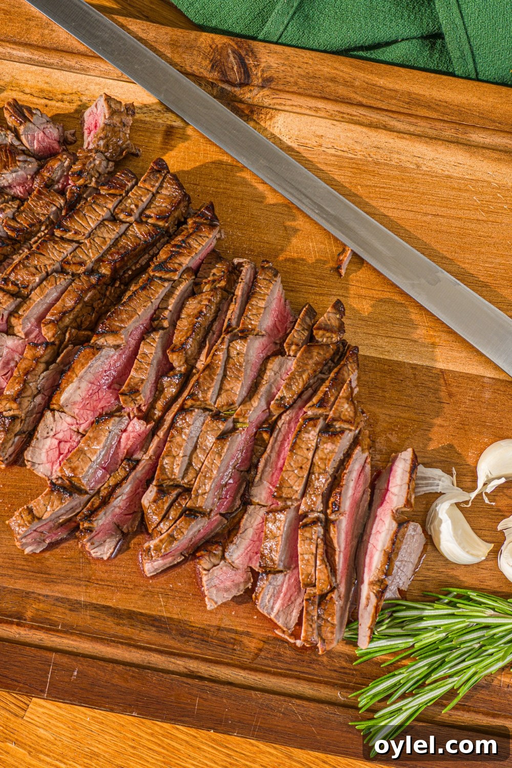 London Broil Marinade Recipe for Tender, Flavorful Steak 11 A wooden board with sliced London broil served with garlic and rosemary. There is a knife on the board.
