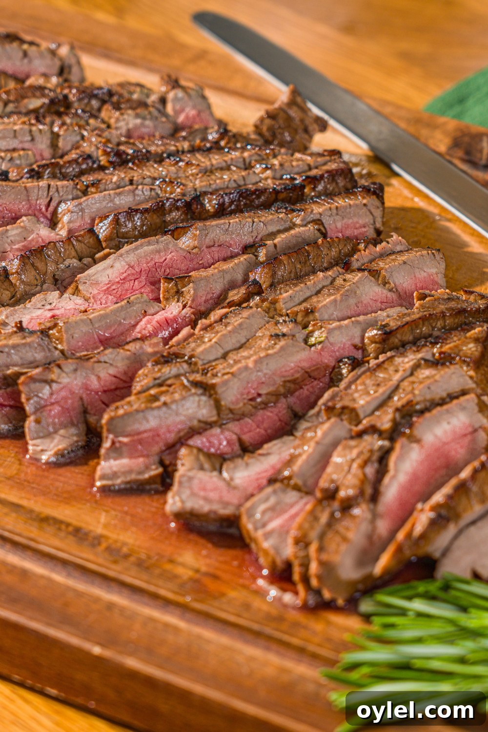 London Broil Marinade Recipe for Tender, Flavorful Steak 12 A wooden board with sliced London broil served with garlic and rosemary. There is a knife on the board.